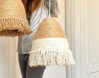 May include: Two handmade macrame lampshades, one in natural jute with a fringe and one in white with a fringe, are held up by a person.