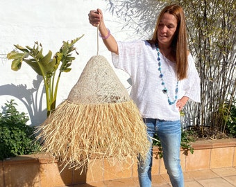 May include: A large, natural fiber pendant light with a woven, straw-like texture. The light is hanging from a white cord and has a fringe of natural fibers around the bottom.