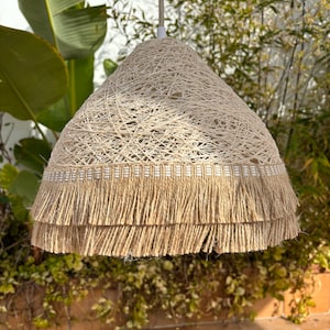 May include: A beige woven pendant light with a double layer of fringe trim. The light is hanging from a white cord.