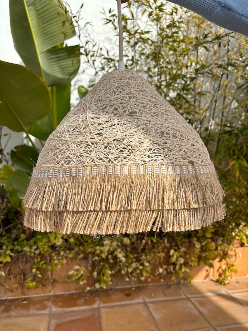 May include: A beige woven pendant light with a double layer of fringe trim. The light is hanging from a white cord.