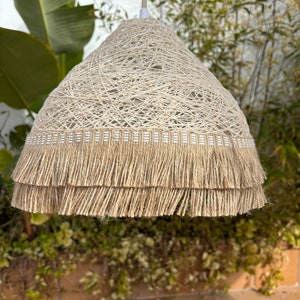 May include: A beige woven pendant light with a double layer of fringe trim. The light is hanging from a white cord.
