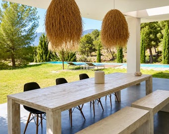 May include: A long rectangular light-colored wooden dining table with two matching wooden benches, three black chairs, and two large, textured, tan-colored hanging pendant lights suspended from the ceiling above the table.