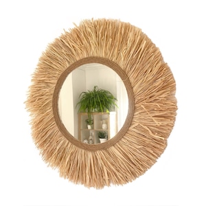 May include: A round mirror with a natural woven straw frame. The mirror has a natural wood finish and a rustic look.