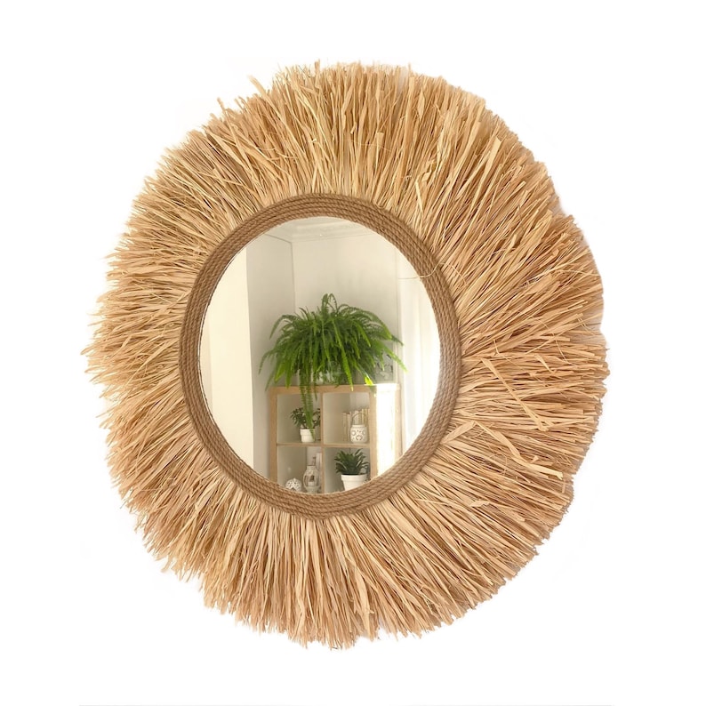 May include: A round mirror with a natural woven straw frame. The mirror has a natural wood finish and a rustic look.