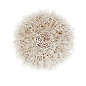 Puede incluir: Decoración mural redonda, blanquecina, con un diseño central de pequeñas conchas claras. La parte exterior está compuesta por material plumoso en capas, creando una forma circular texturizada. Ideal para añadir un toque bohemio natural.