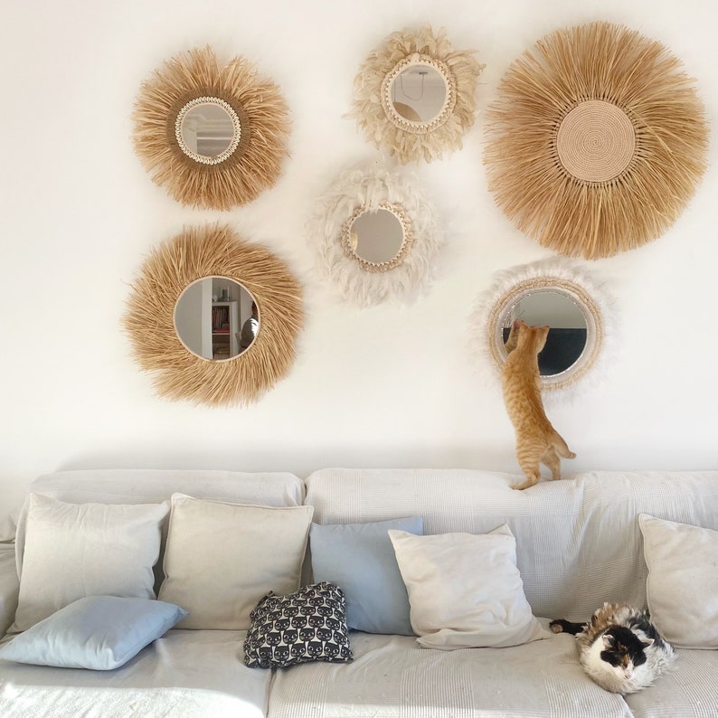 Pode incluir: Um sof&aacute; branco com almofadas e um gato sentado nele. A parede atr&aacute;s do sof&aacute; &eacute; decorada com v&aacute;rios espelhos redondos com molduras de fibra natural.