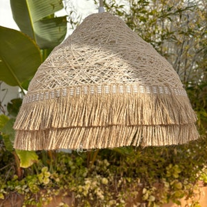 May include: A beige woven pendant light with a double layer of fringe. The light is made of natural fibers and has a rustic, bohemian style.