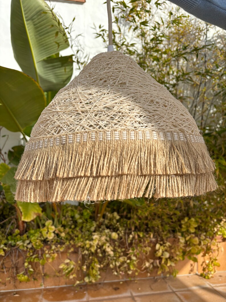 May include: A beige woven pendant light with a double layer of fringe. The light is made of natural fibers and has a rustic, bohemian style.