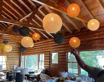 May include: A rustic cabin interior with wooden beams and multiple hanging light fixtures. The lights are made of woven material and are in various shades of brown, beige, and black.
