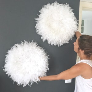 Peut inclure: Deux grandes décorations murales en plumes blanches, l'une étant tenue par la main d'une personne.