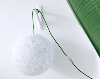 Peut inclure: Un abat-jour rond blanc en forme de corde suspendu à un support mural blanc avec un cordon vert. Le cordon est fixé au mur avec une pince blanche.