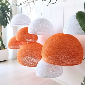 May include: A collection of white and orange string pendant lights hanging from the ceiling. The lights are made of woven string and have a round shape.