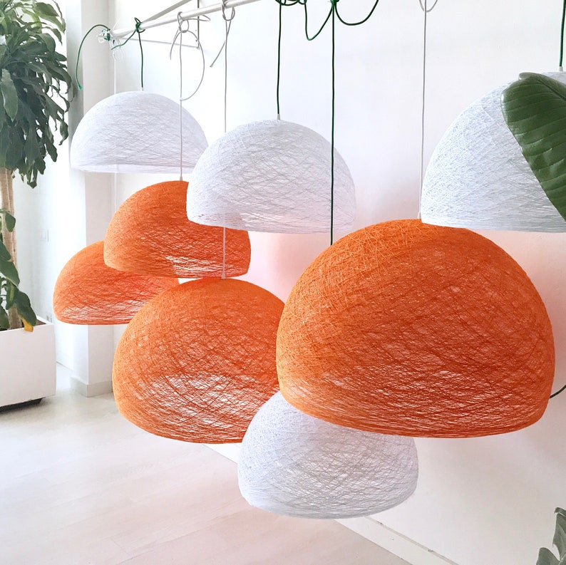 May include: A collection of white and orange string pendant lights hanging from the ceiling. The lights are made of woven string and have a round shape.