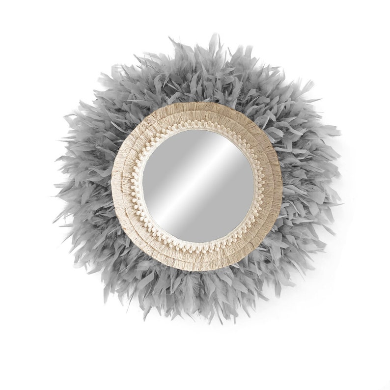 May include: A round mirror with a grey feather trim and a natural fibre frame. The mirror has a simple, modern design.