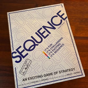 May include: A white and blue board game box titled "SEQUENCE" with the words "It's Fun, It's Challenging, It's Exciting, It's Sequence." The box also states "An Exciting Game of Strategy."