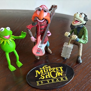 May include: A white ceramic mug with a black handle and the text "But First, Coffee" in a black, handwritten-style font. The mug is on a white surface.