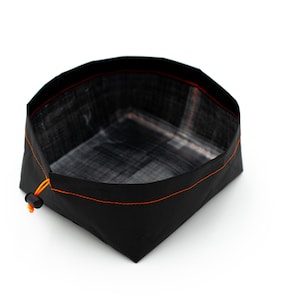 May include: A black foldable bowl with an orange drawstring. The bowl is made of a water-resistant material and is perfect for camping, hiking, or picnics.