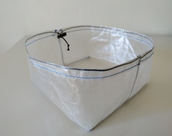 May include: A white, lightweight, rectangular storage bag with a drawstring closure. The bag is made of a thin, translucent material and has a blue and gray seam around the top edge.
