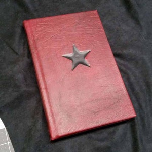 May include: A red leather-bound journal with a black star embossed on the front cover.