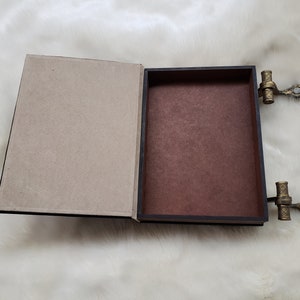 May include: A brown book-shaped box with a hinged lid and gold metal clasps. The box is open, revealing a brown interior.