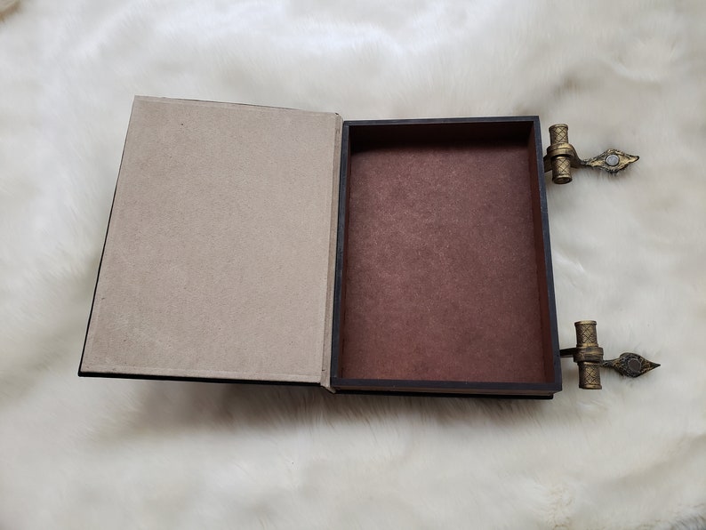 May include: A brown book-shaped box with a hinged lid and gold metal clasps. The box is open, revealing a brown interior.