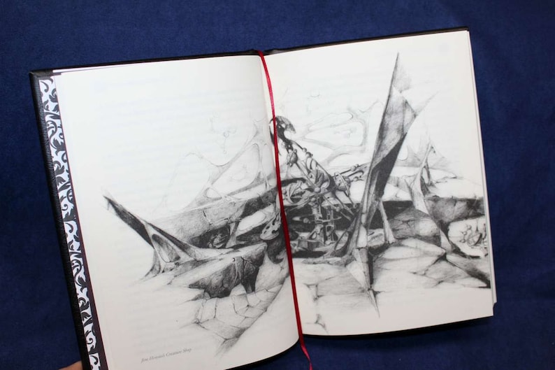 May include: A black and white pencil drawing of a complex, abstract design. The drawing is on a white page in a black bound book.