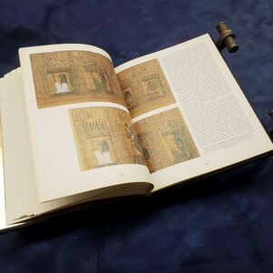 May include: An open book with gold-leaf edges and decorative metal clasps. The pages feature images of ancient Egyptian hieroglyphics and illustrations.
