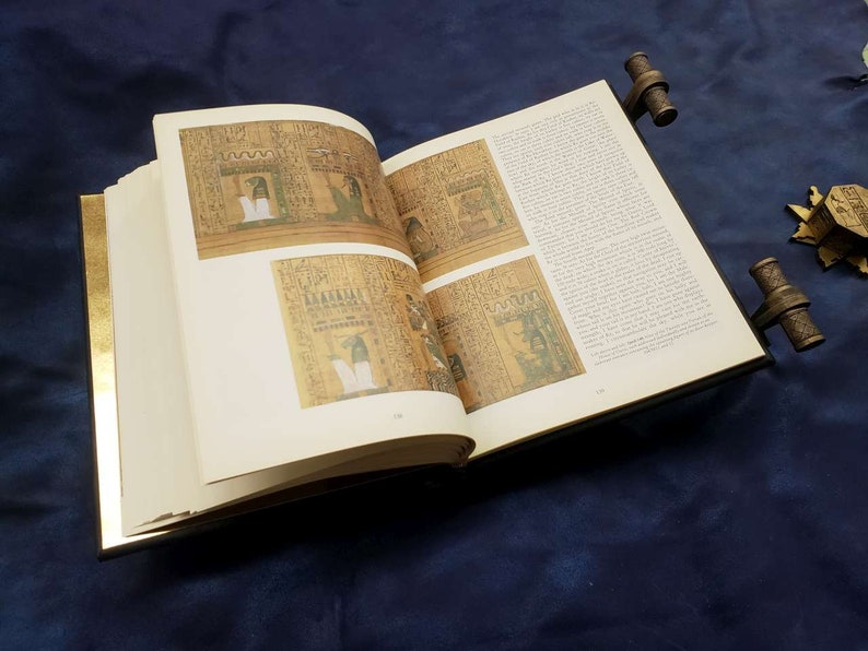 May include: An open book with gold-leaf edges and decorative metal clasps. The pages feature images of ancient Egyptian hieroglyphics and illustrations.