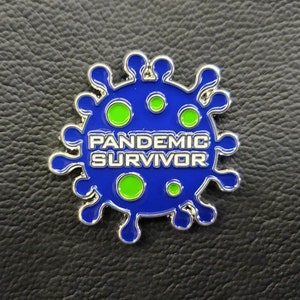 Może przedstawiać: Srebrna szpilka z niebieskim wzorem wirusa i napisem "Pandemic Survivor" białymi literami. Wirus ma zielone koła wewnątrz.