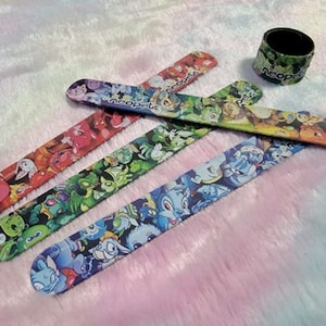 May include: Five colourful plastic bracelets with cartoon characters printed on them. The bracelets are all different designs and colours. One of the bracelets has the word "Neopets" printed on it.