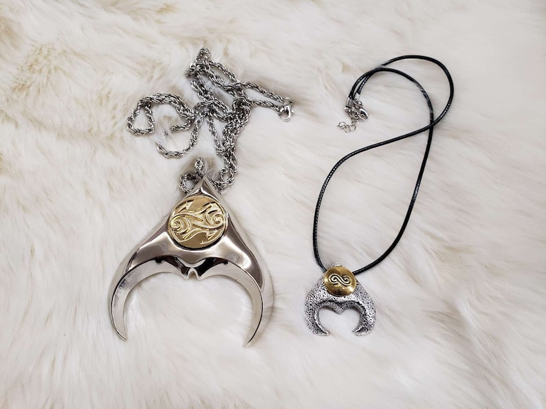 May include: Two silver necklaces with crescent moon pendants. The pendants have a gold-colored design in the center.