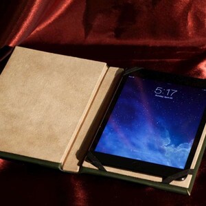 May include: A brown leather tablet case with a green border, open to reveal a black tablet with a blue screen displaying the time 5:17.