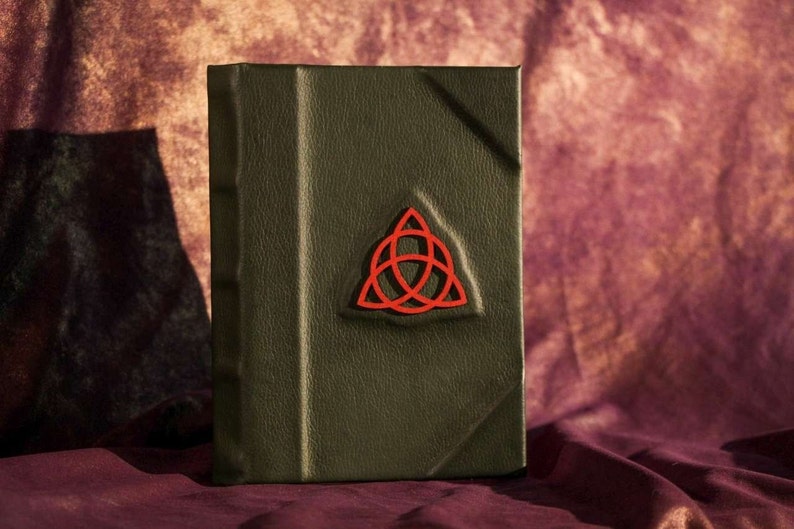 May include: A dark green leather-bound journal with a red, three-dimensional, Celtic knot design on the front cover.