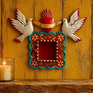 May include: A decorative wall hanging featuring a central red square frame with scalloped edges, painted with green leaves and yellow flowers. Above the frame is a red heart with a yellow banner and two white doves with red-tipped wings.