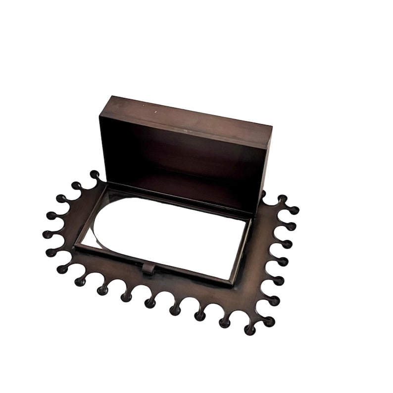 May include: A dark brown, rectangular box with a hinged lid, set on a decorative, scalloped-edge base. The box is open, revealing a white interior. The base and box appear to be made of metal.