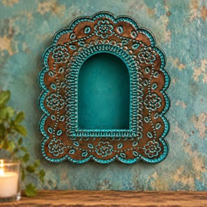 May include: A wall-mounted arched display shelf featuring a metallic bronze finish with vibrant turquoise accents. The frame has a scalloped edge and is decorated with embossed floral patterns and small dots throughout the entire surface.