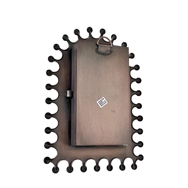 May include: A bronze-colored metal picture frame with a decorative scalloped edge. The back of the frame is visible, showing a rectangular metal plate with a small sticker that reads "Made in Mexico". A metal loop is attached for hanging.