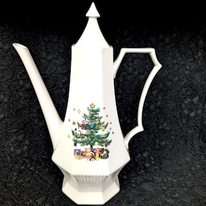 May include: White ceramic coffee pot with a Christmas tree design. The pot features a tall, pointed lid, a long spout, and a decorative handle. The Christmas tree is decorated with ornaments and presents.
