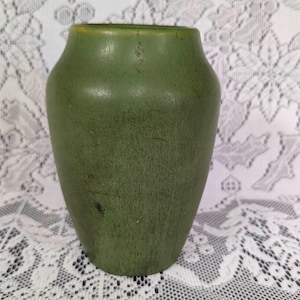 May include: A green ceramic vase with a slightly textured surface. The vase has a rounded body and a narrow neck. The color is a muted, earthy green, and the vase appears to be vintage.