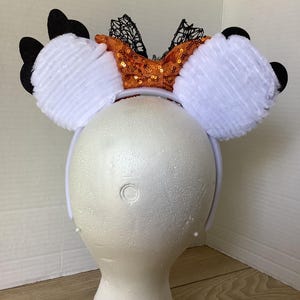 Op de afbeelding: Witte, pluche muizenoren met een oranje en zwarte pailletten strik. De strik heeft zwarte kant accenten.