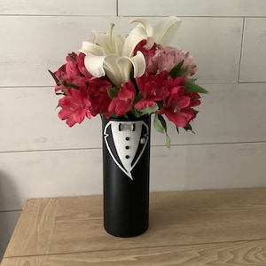 May include: A black vase with a white tuxedo design painted on it. The vase is filled with white lilies and pink alstroemeria flowers.