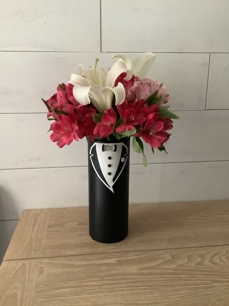 May include: A black vase with a white tuxedo design painted on it. The vase is filled with white lilies and pink alstroemeria flowers.