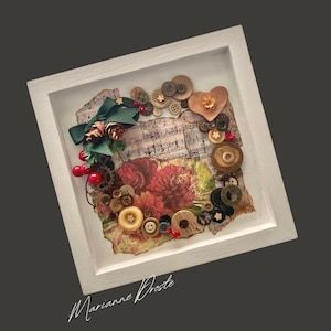 May include: A framed mixed-media artwork featuring a collage of vintage buttons, sheet music, and floral elements. The composition includes a green bow, pinecones, and red berries, all set within a white shadow box frame. The artist's signature is at the bottom.