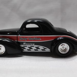 May include: Black Harley-Davidson Racing model car with red and white accents. The car features a classic design with a checkered flag pattern and the Harley-Davidson Racing logo. The car has silver wheels.