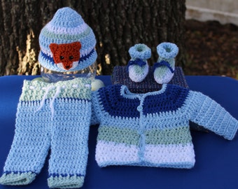 May include: A crocheted baby outfit in blue, white, and green with a fox-themed hat. The outfit includes a cardigan, pants, and booties.