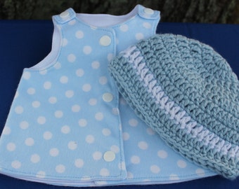 May include: A light blue sleeveless top featuring a white polka dot pattern with white snap buttons down the front, paired with a light blue and white crocheted beanie hat. The top has a white interior lining and a simple, structured design.