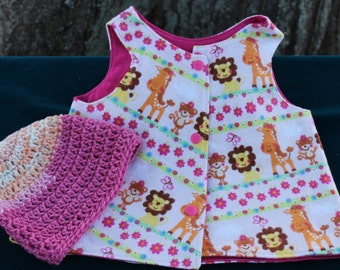 May include: A pink and white sleeveless vest with a button closure and a colorful animal print. The vest has a pink crocheted hat with a peach and white ombre design.