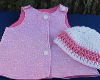 May include: A pink and white polka dot baby vest with a white crocheted hat with a pink trim.