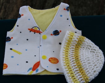 May include: A white and yellow baby vest with a space theme print, featuring planets, stars, rockets, and a UFO. It has yellow buttons and a matching white and yellow crocheted hat.
