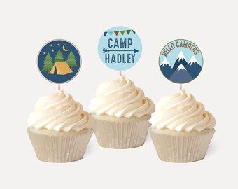 May include: Three cupcakes with blue and green camping themed cupcake toppers. The toppers feature a tent, trees, a moon, stars, mountains, and the text "Camp Hadley" and "Hello Campers".